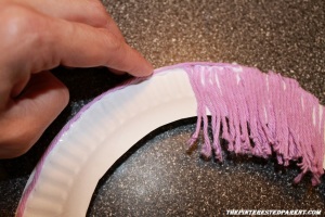 After you have placed your bangs, add a strand of yarn on the out edge of the plate following the curve of the plate about a 1/4 of the way down & then let the yarn hang straight down & cut to desired length,